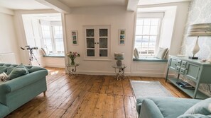 Una sala de estar acogedora con piso de madera, un sofá color esmeralda, una mesa de vidrio y un rincón con ventanales y vistas.