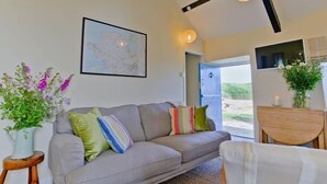 Un salón con un sofá gris, cojines coloridos, un mapa en la pared y vistas al exterior.