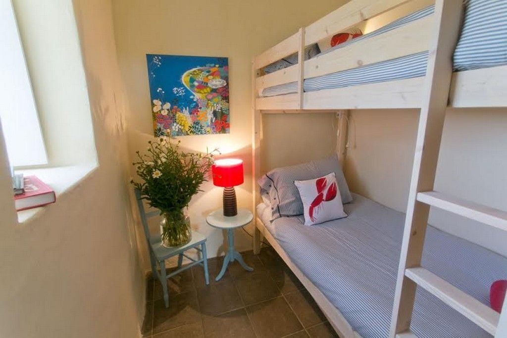 Une petite pièce agréable, avec des lits superposés, une petite table avec une lampe et un tableau au mur.