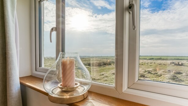 A candle in a glass holder on a wooden surface by a window with a view of a field and sheep. - Pandy Aberffraw -  a dog that sleeps 4 guests  in 2 bedrooms (Ty Croes)