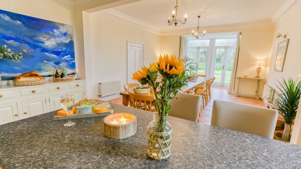 A spacious kitchen with a granite countertop, a large painting, and a vase with sunflowers.