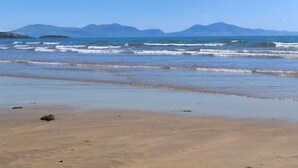 A beach with waves, a clear sky, and mountains in the background.