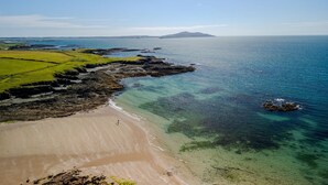Paisagem costeira com praia arenosa, águas cristalinas e afloramentos rochosos.