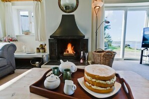 Una sala de estar acogedora con chimenea, una mesa de comedor con un pastel y vistas al exterior.