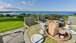 A round wooden table with a basket of bread, a jug of milk, and a cup of coffee. - Tan Y Bryn -  a sea view that sleeps 10 guests  in 5 bedrooms (Llanddona)