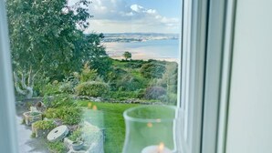 A view from a window overlooking a garden with a body of water and distant land. - Tan Y Bryn -  a sea view that sleeps 10 guests  in 5 bedrooms (Llanddona)