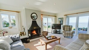 A cozy living room with a fireplace, comfortable seating, a television, and a view of the outdoors. - Tan Y Bryn -  a sea view that sleeps 10 guests  in 5 bedrooms (Llanddona)