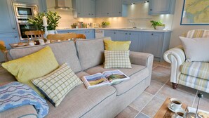 A cozy living room with a sofa, a coffee table, and a dining area with a chair and table. - Afon Menai -  a hot tub that sleeps 4 guests  in 2 bedrooms (Llanfairpwllgwyngyll)