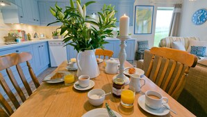A breakfast setting with a wooden table, chairs, a potted plant, a white candle, and breakfast items like croissants, orange juice, and coffee. - Afon Menai -  a hot tub that sleeps 4 guests  in 2 bedrooms (Llanfairpwllgwyngyll)