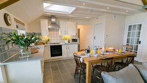 Eine moderne Küche mit weißen Schränken, ein Essbereich mit Holztisch und -stühlen und ein graues Sofa.