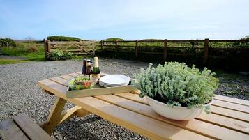 A wooden picnic table with a salad bowl, plates, and bottles of drinks.
