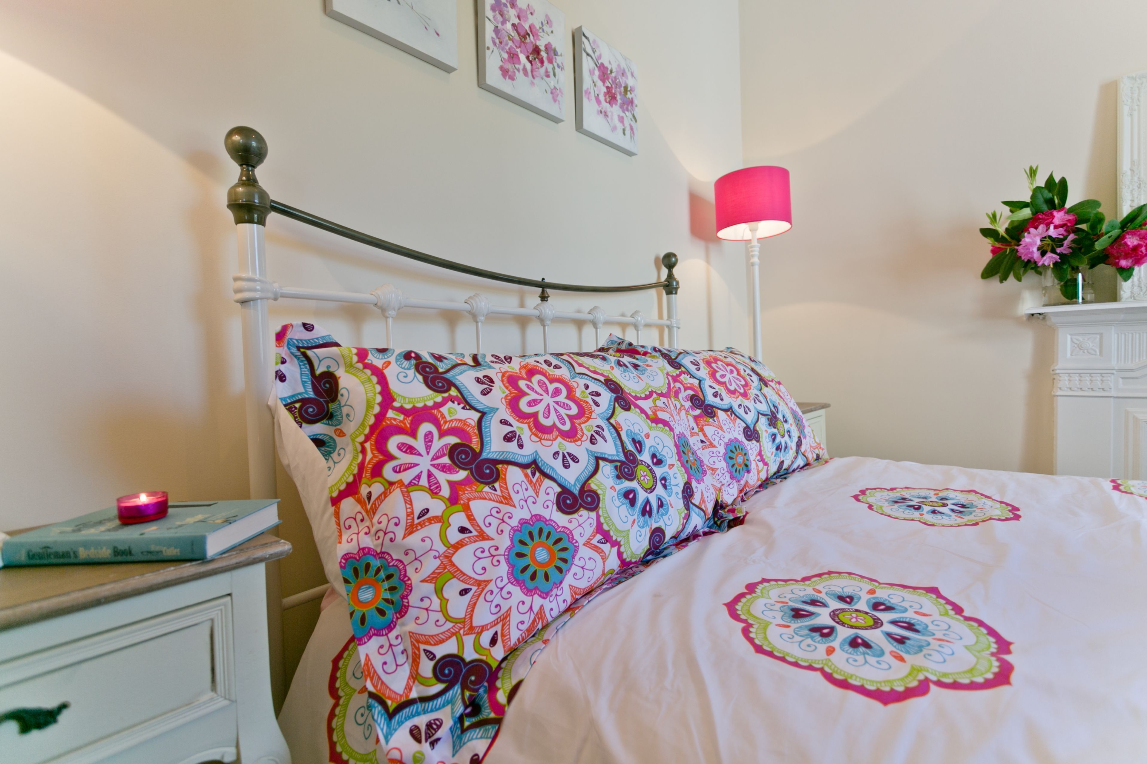 A bed with colorful floral bedding, a bedside table with a book, and a lamp.