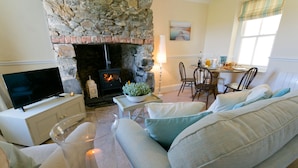 Una sala de estar acogedora con chimenea de piedra, televisión, comedor con sillas y sofá con cojines.