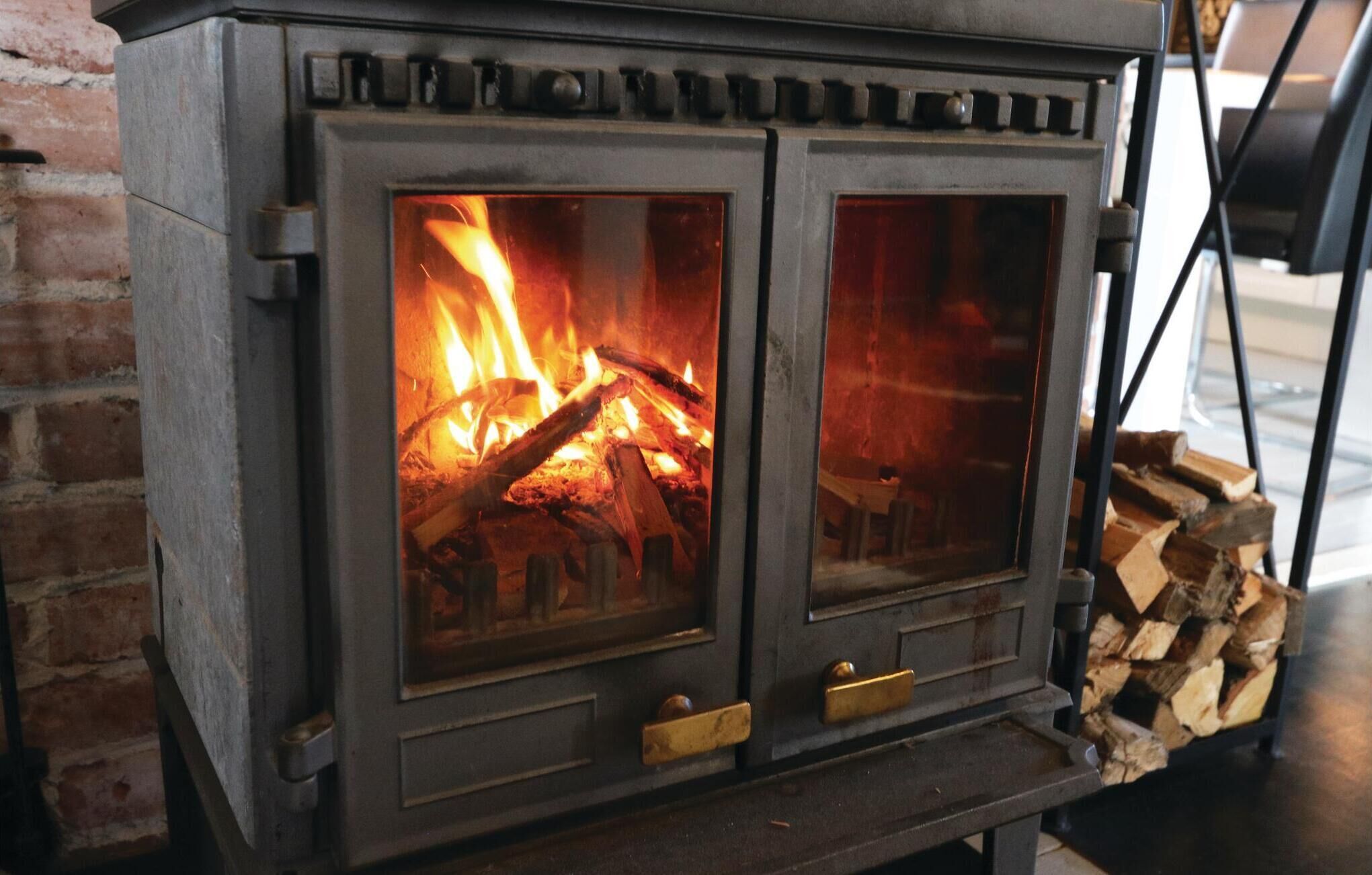 A wood-burning stove with two glass doors, a metal handle, and a brick wall in the background.