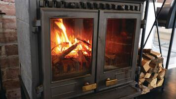 A wood-burning stove with two glass doors, a metal handle, and a brick wall in the background.