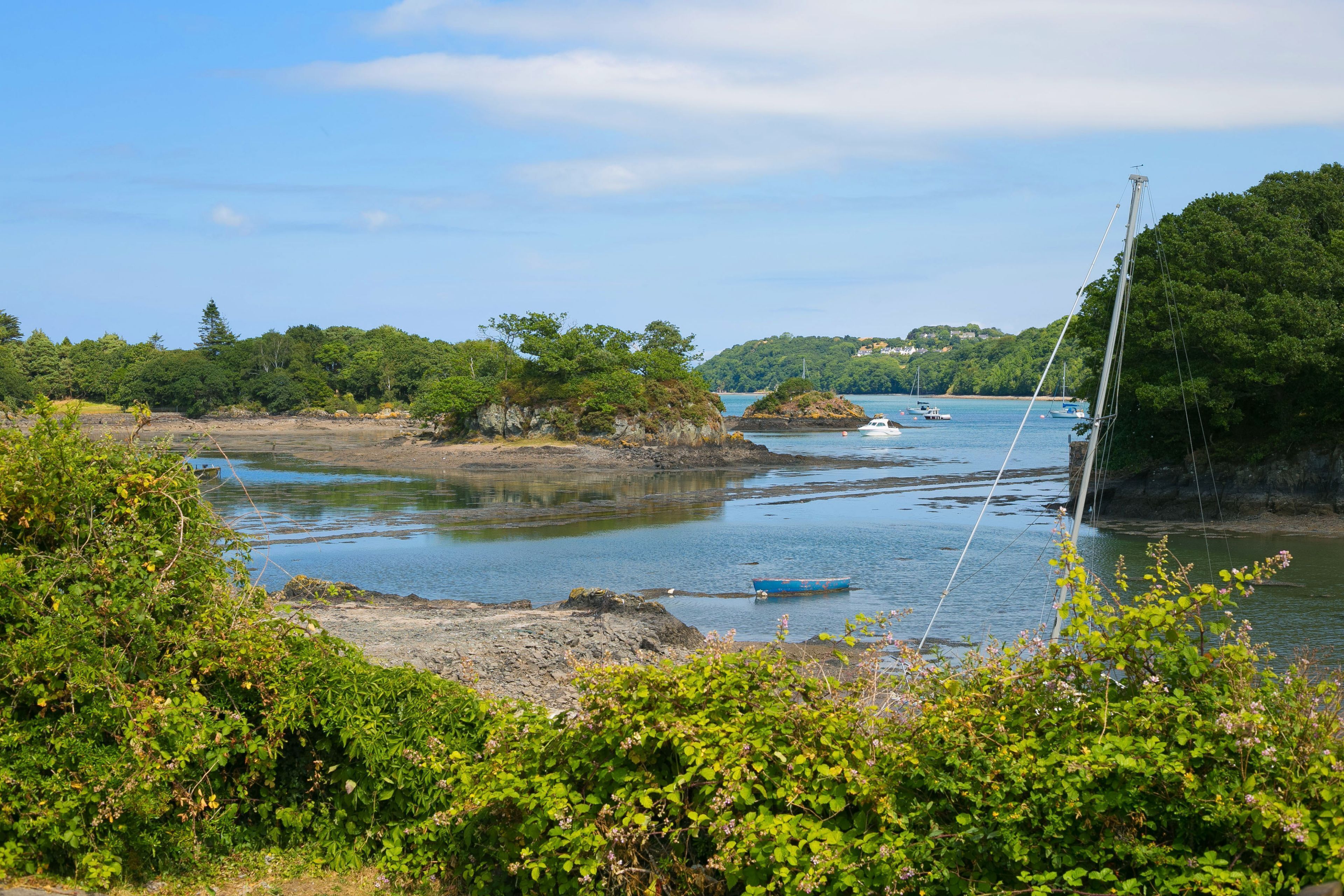 Un paysage côtier avec une rivière paisible, des bateaux et une végétation luxuriante.