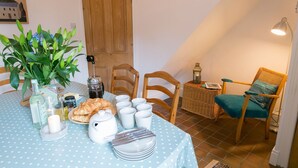 A dining area with a polka dot tablecloth, wooden chairs, a wicker side table, and a lamp. - Hyfrydle -  a coastal that sleeps 6 guests  in 3 bedrooms (Beaumaris)