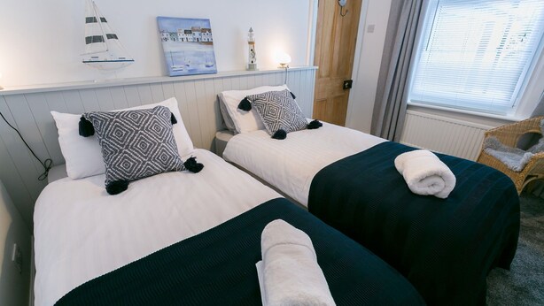 Two single beds with white and dark green bedding, a painting of a coastal scene, and a small sailboat model on the wall. - Hyfrydle -  a coastal that sleeps 6 guests  in 3 bedrooms (Beaumaris)