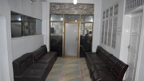 A reception area with two leather sofas, a patterned floor, a glass door with a metal gate, and a white wall with a decorative panel. - Royal Inn Guest House (Mekhtar)