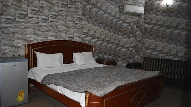 A bedroom with a wooden bed, white bedding, a grey blanket, a small fridge, and a radiator. - Royal Inn Guest House (Mekhtar)