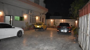 A parking area with three cars parked in front of a building with multiple windows and outdoor lighting. - Royal Inn Guest House (Mekhtar)