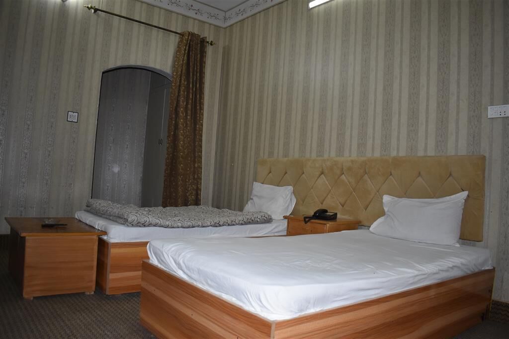 A hotel room with two beds, a wooden nightstand, a telephone, and a curtain.
