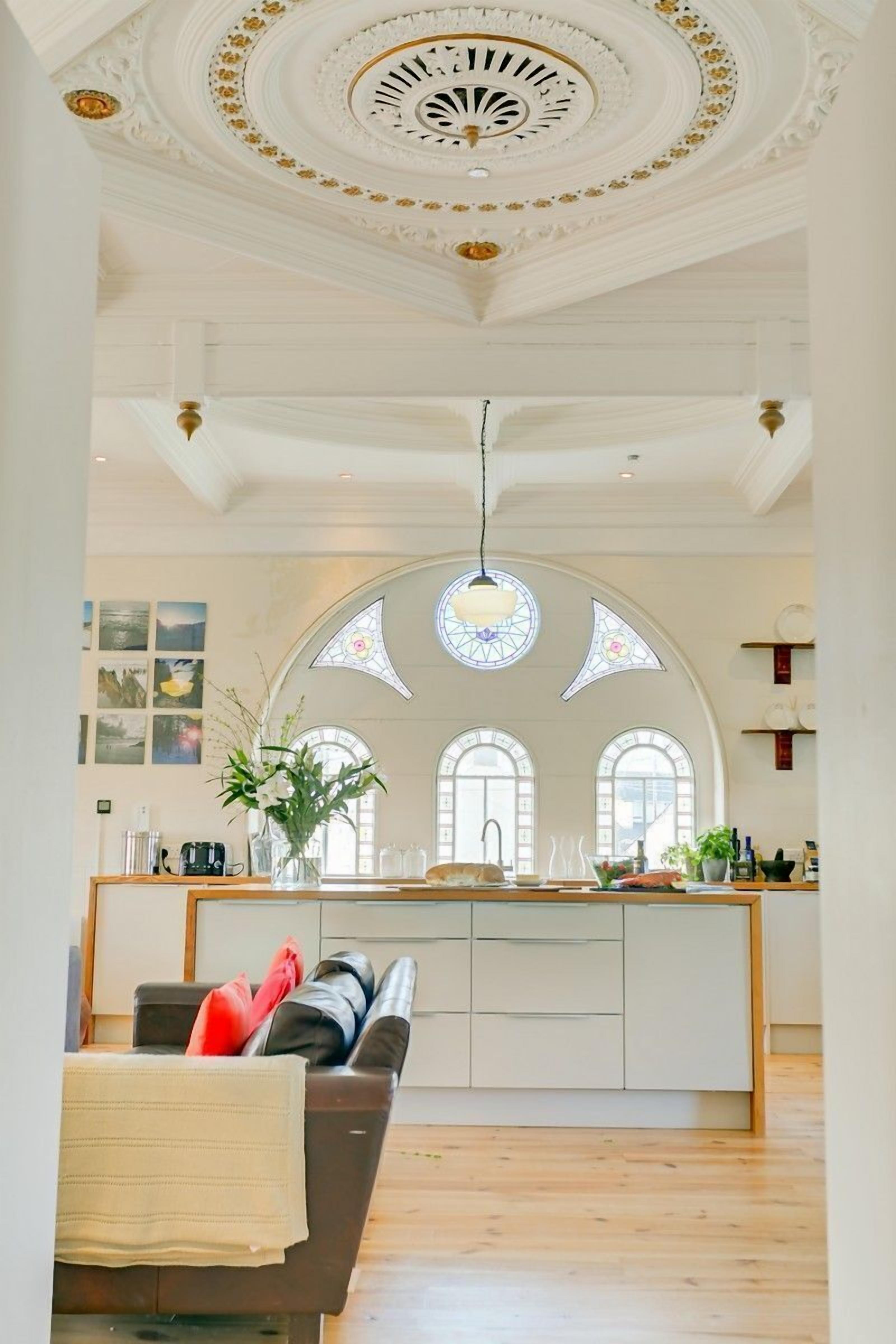 A spacious living area with a high ceiling, a central island with a sink, and a seating area with a couch and chairs.