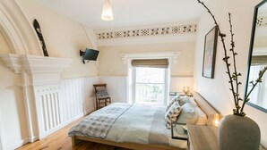 A bedroom with a bed, a chair, a bedside table with a lamp, a window, and a decorative wall piece. - Cwyfan -  a dog that sleeps 8 guests  in 4 bedrooms (Ty Croes)