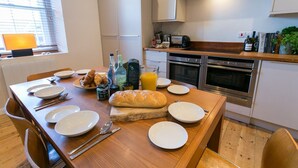 A modern kitchen with a wooden dining table set for breakfast, including croissants, bread, and orange juice. - Coron -  a dog that sleeps 6 guests  in 3 bedrooms (Ty Croes)