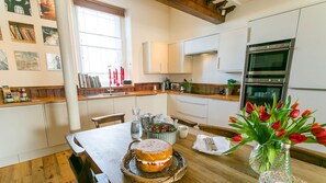 Una cocina moderna con armarios blancos, encimera de madera y una mesa de comedor preparada para dos personas. Hay un ramo de tulipanes sobre la mesa.
