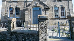 Un edificio histórico de piedra con una entrada central, ventanas de arco y una imponente torre del reloj.