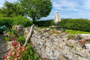 Un jardín con pared de piedra, una mesa de picnic y una parrilla.