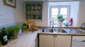 A kitchen with a wooden countertop, a sink, a potted plant, and a shelf with kitchenware.