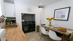 A modern kitchen with a wooden countertop, white chairs, a dining table, and a black oven. - Shell Cottage -  a dog that sleeps 4 guests  in 2 bedrooms (Menai Bridge)