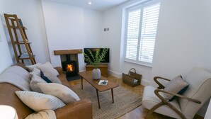 A cozy living room with a fireplace, a sofa, a coffee table, and a TV. - Shell Cottage -  a dog that sleeps 4 guests  in 2 bedrooms (Menai Bridge)