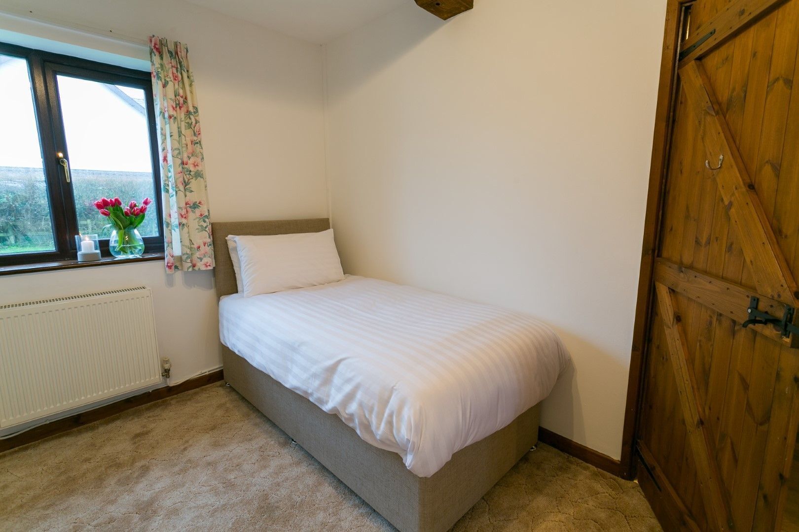 A single bed in a room with a window, a radiator, and a wooden door.