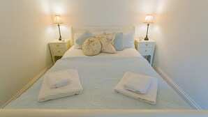 A neatly made bed with two pillows, two bedside tables with lamps, and folded towels on the bed.