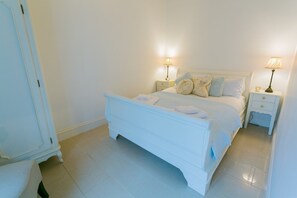 A white four-poster bed with a matching nightstand, two bedside lamps, and a small table with a lamp.