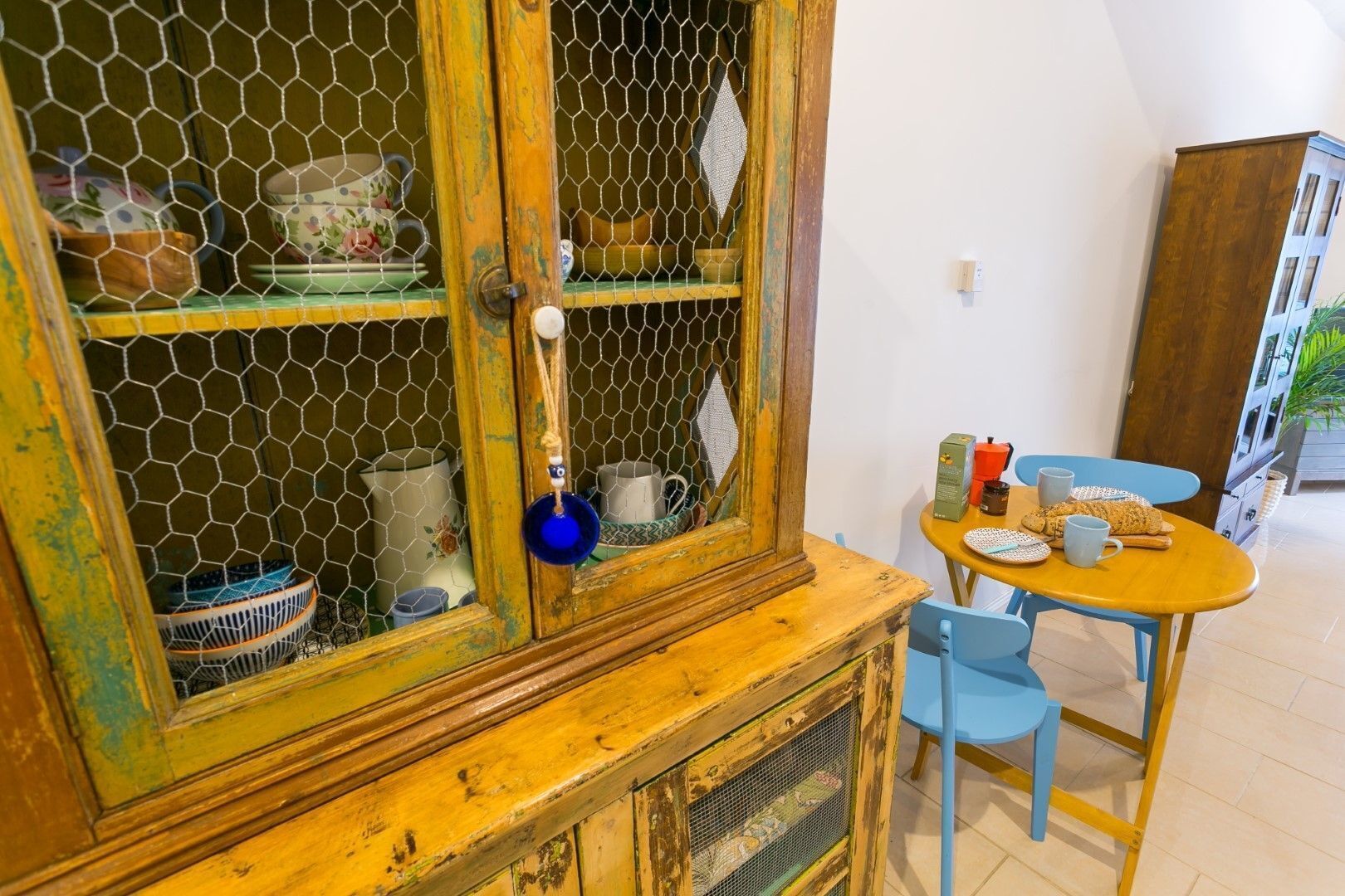A room with a wooden cabinet with glass doors, a small table with chairs, and various items on the table.