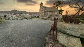 A stone building with a stone facade, a paved driveway, and a horse statue. - Tal Y Bont Uchaf Stables -  a hot tub that sleeps 16 guests  in 5 bedrooms (Bangor)