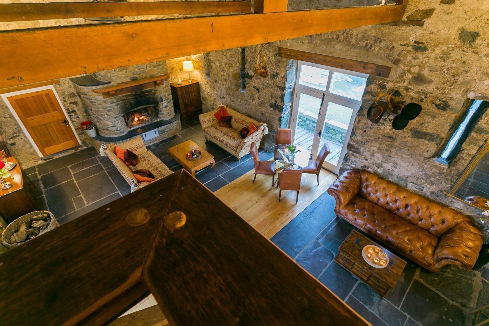 A stone-floored living room with a fireplace, leather sofa, and a dining area with chairs and a table.