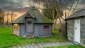 A log cabin with a steeply pitched roof, a front door with a glass panel, and a small porch. - Tal Y Bont Uchaf Stables -  a hot tub that sleeps 16 guests  in 5 bedrooms (Bangor)