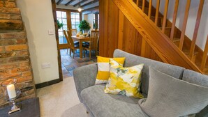 Ein gemütliches Wohnzimmer mit grauem Sofa, einer Holztreppe und einem Essbereich im Hintergrund.
