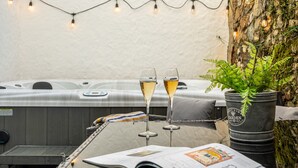Ein Whirlpool mit Holzterrasse, zwei Sektgläsern, einem Buch und einem Farn.