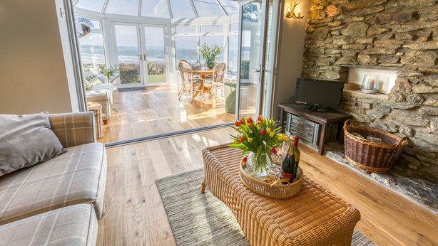A cozy living room with a sofa, a wicker coffee table with a vase of flowers, a stone wall, and a fireplace.