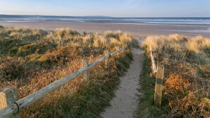 A sandy path leading to a beach with a wooden fence on one side.