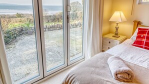 A bedroom with a large window overlooking a rocky landscape and the sea.
