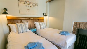 Une chambre double avec deux lits, chacun agrémenté de draps blancs et d’oreillers à rayures, d’une tête de lit en bois et d’un tableau au-dessus des lits.