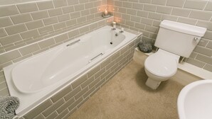 A bathroom with a bathtub, toilet, and a small shelf with candles. - Sea Bell -  a coastal that sleeps 6 guests  in 3 bedrooms (Holyhead)