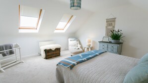 A bedroom with a large bed, a chair, a dresser, a radiator, and a skylight. - Sea Bell -  a coastal that sleeps 6 guests  in 3 bedrooms (Holyhead)